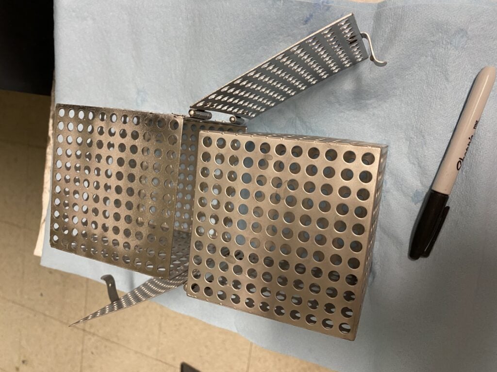 Two small perforated metal boxes, which will be snapped together to make a single, larger box for holding a 3D printed part while its support material is dissolved in sodium hydroxide.